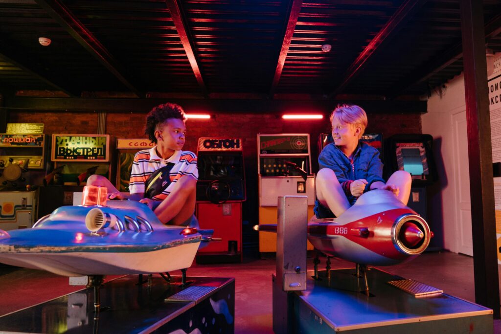 Two teenagers enjoying a playful moment on arcade rides in a vibrant amusement setting.
